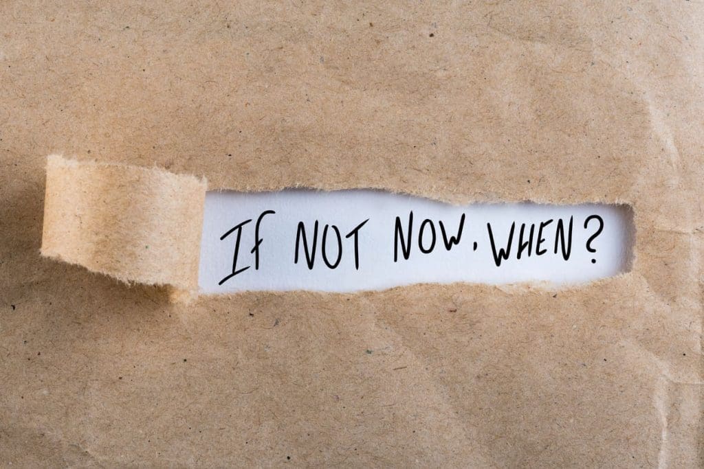 A piece of brown paper is torn open to reveal the handwritten phrase, “If not now, when?” on a white background.