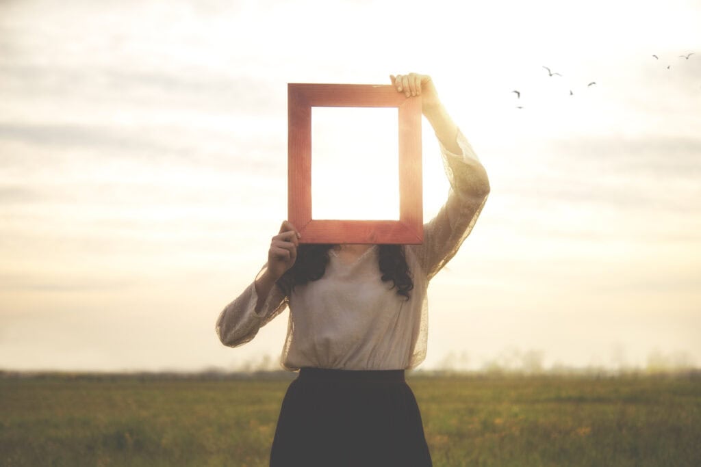 A woman holding a red frame in an open field during sunset, symbolizing mindfulness and wellness.