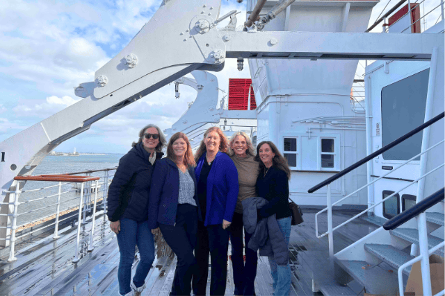 5 women dressed in winter gear pose on the deck of the Queen Mary in Long Beach