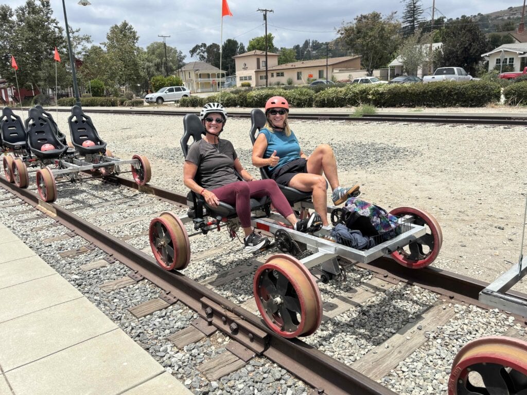 Two women riding a pedal-powered rail bike on a railway track outdoors.