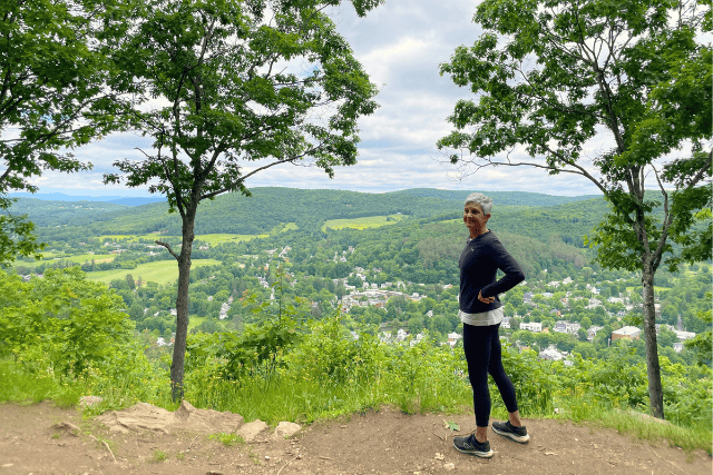 Lisa stands at a hilltop in nature overlooking a valley below